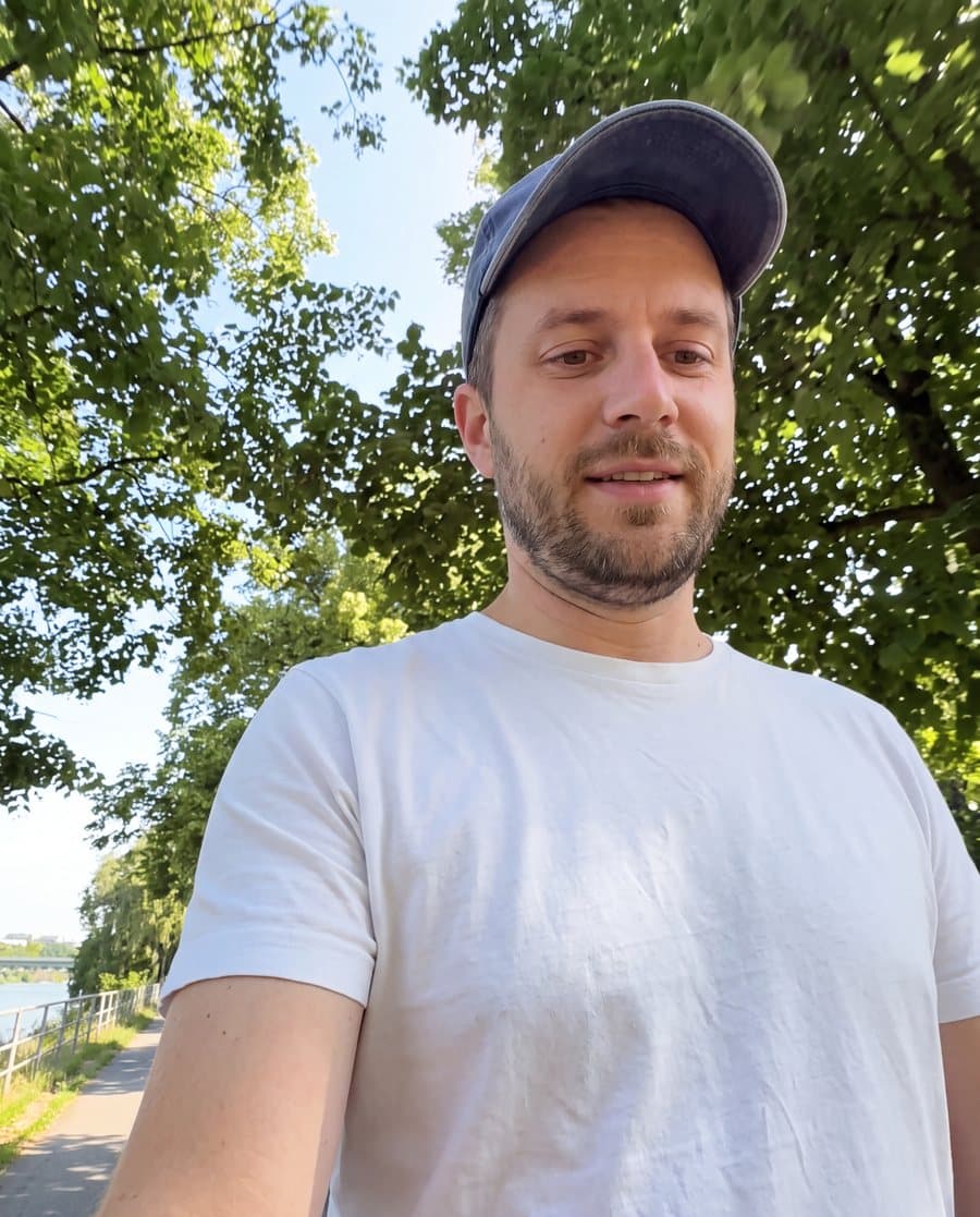 What the phone shows: a man in an orange cap records a video review while walking by the river